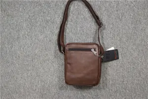 Detail view of brown vertical PU leather messenger bag showing zipper pocket and brand hangtag.