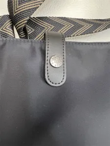 Nylon crossbody bag detail shot, featuring geometric pattern strap and metal snap button.