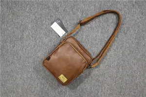 Detail view of brown vertical messenger bag, featuring durable leather texture and zipper pocket.
