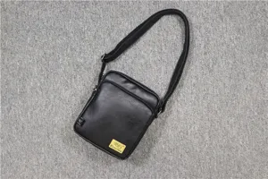 Detail view of black vertical PU leather messenger bag featuring adjustable strap and zipper pocket.