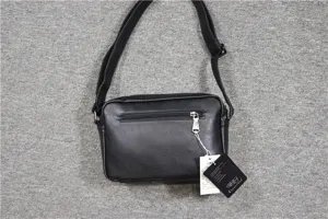 Detail view of the black soft leather cross-body messenger bag showing zipper and brand tag.