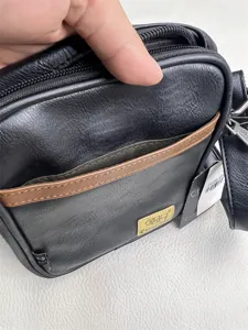 Detail view of black vertical crossbody bag with front pocket, zipper closure and strap.