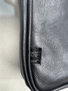 Detailed close-up view of black leather crossbody bag texture and branded side woven tag.