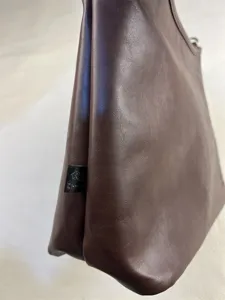 Close-up detail of dark brown leather shoulder tote bag side texture and stitched seam label.