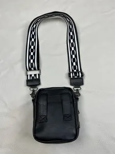 Detailed view of men's black vertical crossbody bag with black white geometric wide strap.