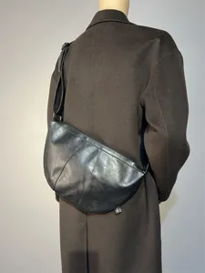 Detail view of black leather crescent crossbody bag showing texture and adjustable strap.
