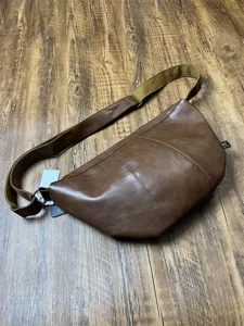 Detail view of the brown leather crossbody dumpling bag, showing the durable texture and strap.
