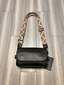 Black crossbody bag detail, woven strap, metal buckles, stylish everyday accessory.