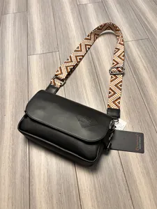 Detailed view of black leather crossbody bag with ethnic woven strap and metal hardware.