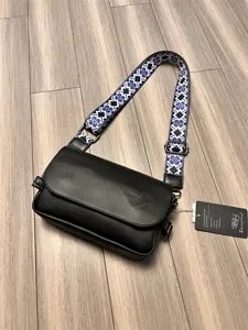 Detail view of stylish black cross-body bag featuring blue patterned strap and hardware.