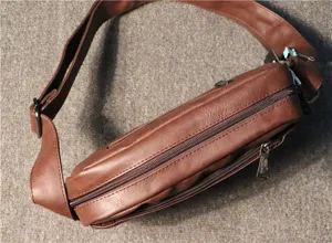 Close-up detail of brown leather messenger bag, showing texture, dual zippers and wide strap.