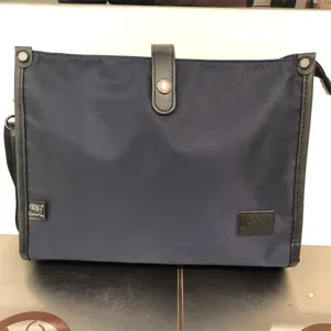 Detalle de bolso bandolera de nailon azul oscuro con ribete de cuero y cierre de botón.