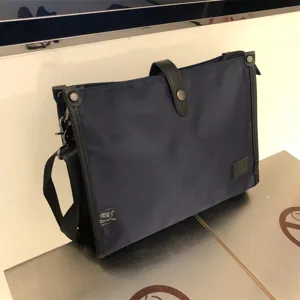 Vista detallada del bolso mensajero de nailon azul marino, mostrando textura, etiqueta y herrajes.