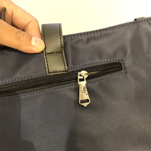 Detalle de bolso de nylon azul oscuro con cremallera metálica resistente y tirador de marca.