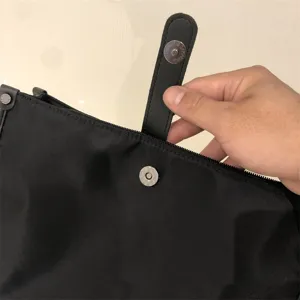 Detalle de bolso bandolera negro de nylon con solapa de cuero, cremallera y botón de presión.