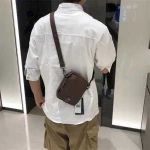 Detail shot of brown leather vertical crossbody bag worn by model, showing casual style.
