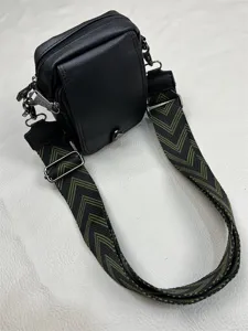 Detail view of men's black crossbody bag with wide green chevron patterned strap and hardware.