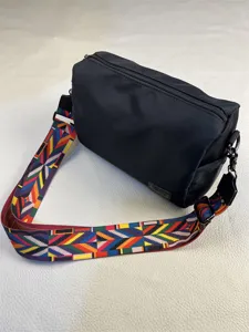 Detail view of black nylon crossbody bag featuring colorful geometric woven strap and zipper.