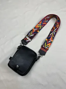 Close-up of black vertical crossbody bag with colorful woven strap and metal snap closure.