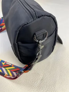 Detailed shot of black nylon cylinder shoulder bag with colorful geometric strap and metal hardware.