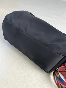 Detailed view of a black nylon cylindrical crossbody bag with colorful striped strap, perfect.