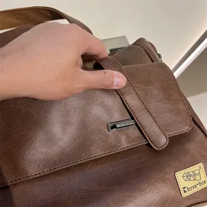 Vue détaillée du sac marron pour hommes, montrant la texture cuir et la boucle métallique.