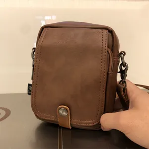 Detail view of men brown vertical shoulder crossbody bag, casual soft leather design.
