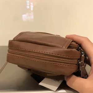 Detail shot of brown soft leather mini cross body bag with multiple zipper layers and metal pulls.