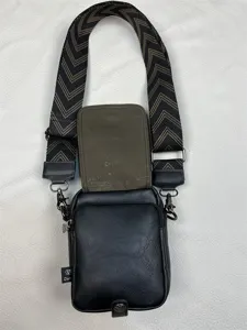 Detailed view of the black leather vertical crossbody bag featuring wide patterned strap and hardware.