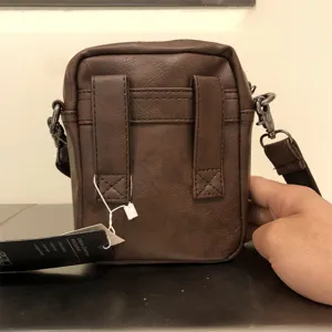 Detail shot of brown leather mens vertical crossbody bag showing back design and brand tag.