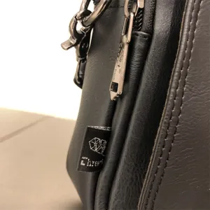 Close up detail of black leather cross body bag side showing metal zipper hook and brand label text