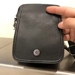 Black soft leather vertical crossbody bag detail view showing magnetic snap button and texture.