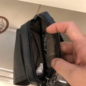Black synthetic leather vertical crossbody bag for men featuring multiple inner compartments.