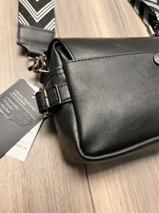 Detail shot of black leather crossbody bag featuring patterned strap and metal hardware.