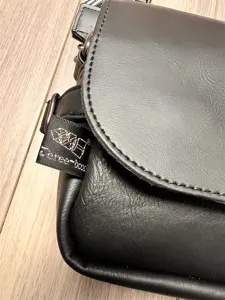 Detail view of black leather messenger bag, showing texture, flap design, and strap.
