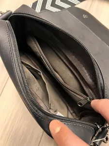 Detailed view of dark grey crossbody bag interior with multiple zipper compartments.