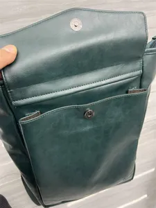 Dark green leather backpack detail view with magnetic closure and front pocket storage.