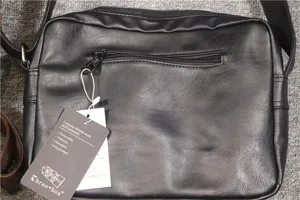 Detail view of the black leather crossbody bag featuring front zipper pocket and brand tag.