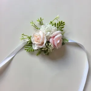 Detalle de corsé de muñeca de rosa artificial rosa y blanca con hojas verdes y cinta.