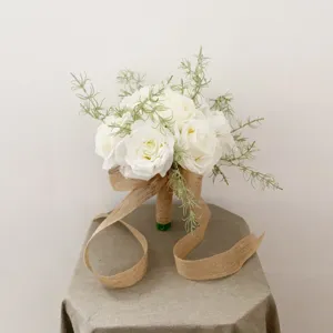 Gros plan détaillé d'un bouquet de mariée en roses blanches artificielles et ruban de jute.
