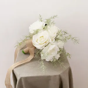 Bouquet de mariée de roses artificielles blanches avec feuillage vert et ruban de jute.