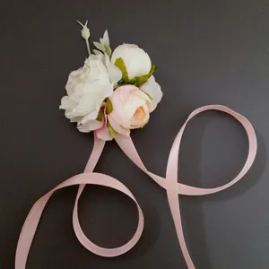 Close-up detail of artificial pink and white flower corsage with long ribbons for wedding.