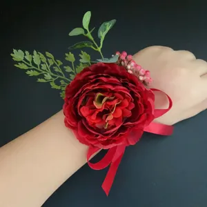 Red artificial flower wrist corsage with green leaves and ribbon for wedding and photography.