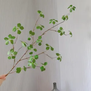 Detailed close-up of artificial green plant branch with delicate leaves for floral arrangement decor.