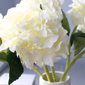 Primo piano di ortensia artificiale bianca in seta con foglie verdi in vaso elegante.