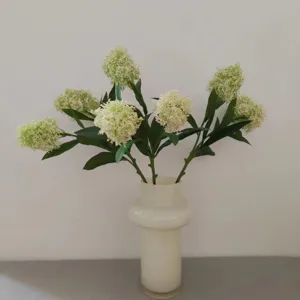 Detailed view of artificial skimmia flower branches with white berries in a modern white vase.