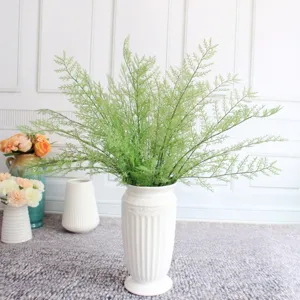 Detailed view of artificial fern green plant foliage leaves in a white vase for floral decor.