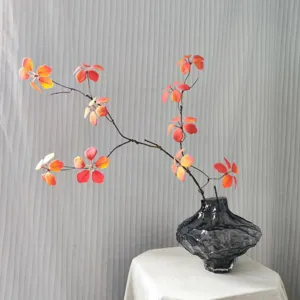 Artificial autumn red leaves branch in dark grey glass vase, home decor floral arrangement.
