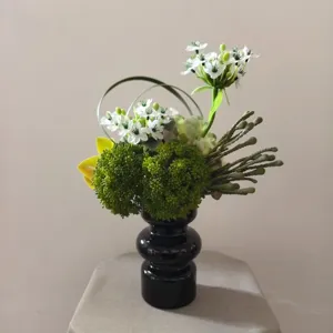 Artificial floral arrangement detail showcasing mixed green plants and white blooms in a black vase.
