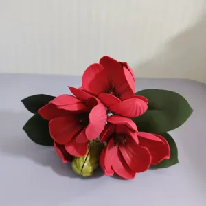 Vue détaillée d'un bouquet de fleurs de magnolia artificielles rouges avec des feuilles vertes.